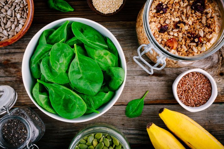 17 Surprising Spinach Nutrition Facts & Health Benefits; Ingredients for green spinach smoothies: bananas, granola, chia seeds on wooden background