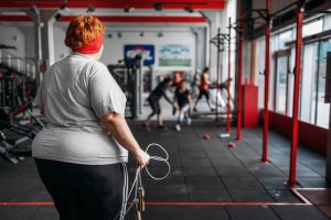 Worldwide Obesity Statistics, Facts & Trends; Fat sweaty woman, fit training with rope in gym