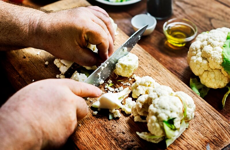 34 High Protein Vegetables You Probably Already Eat; Closeup of hands with knife cutting fresh organic cauliflower