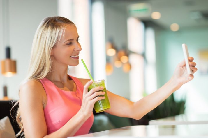 Complete Guide To Smoothies: 200+ Recipes, Diets, Tutorials & Videos; woman with smartphone taking selfie at restaurant