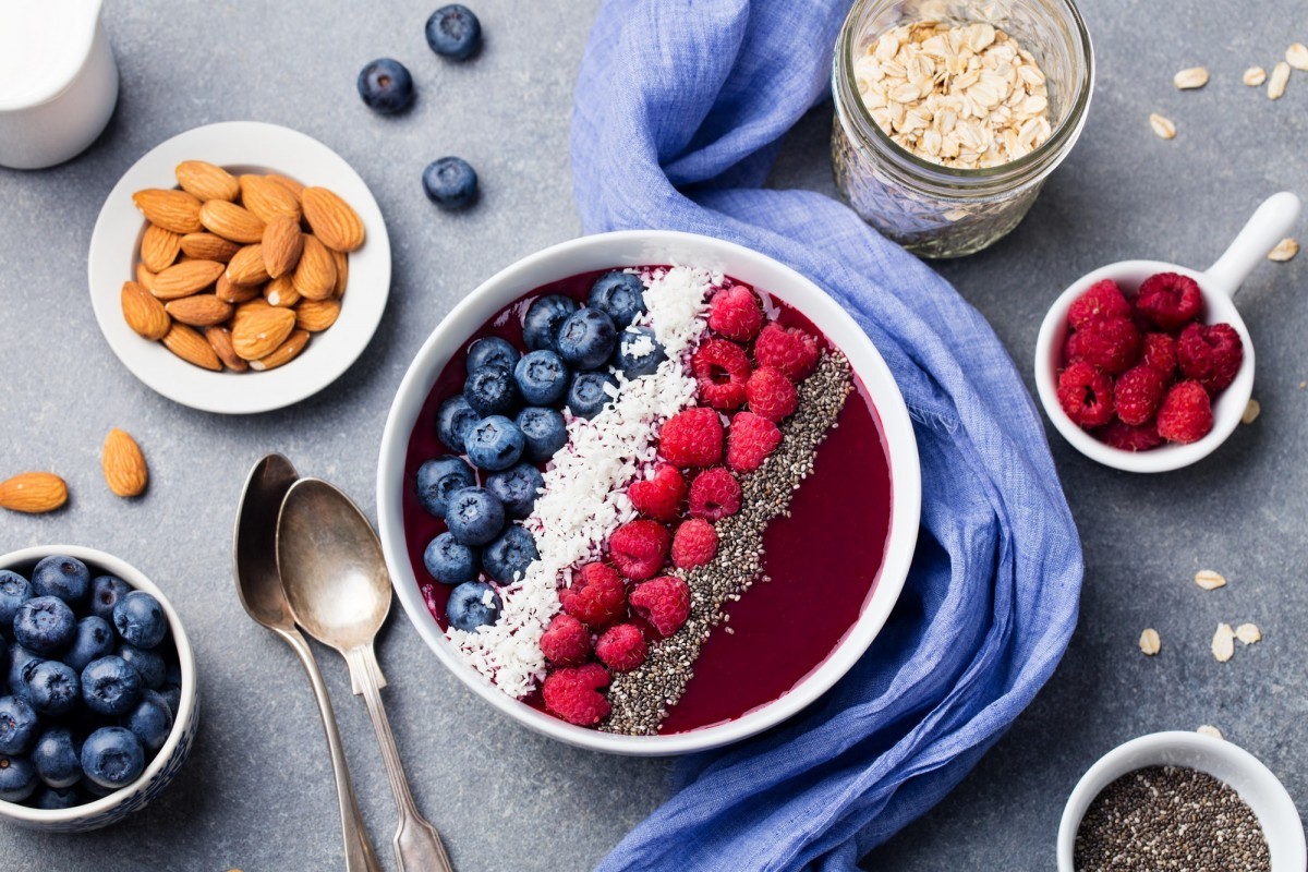 112 Best Smoothie Toppings To Create The Wow Factor; Smoothie Bowl with Fresh Raspberry, Blueberry, Coconut Flakes and Chia Seeds. Grey Background.