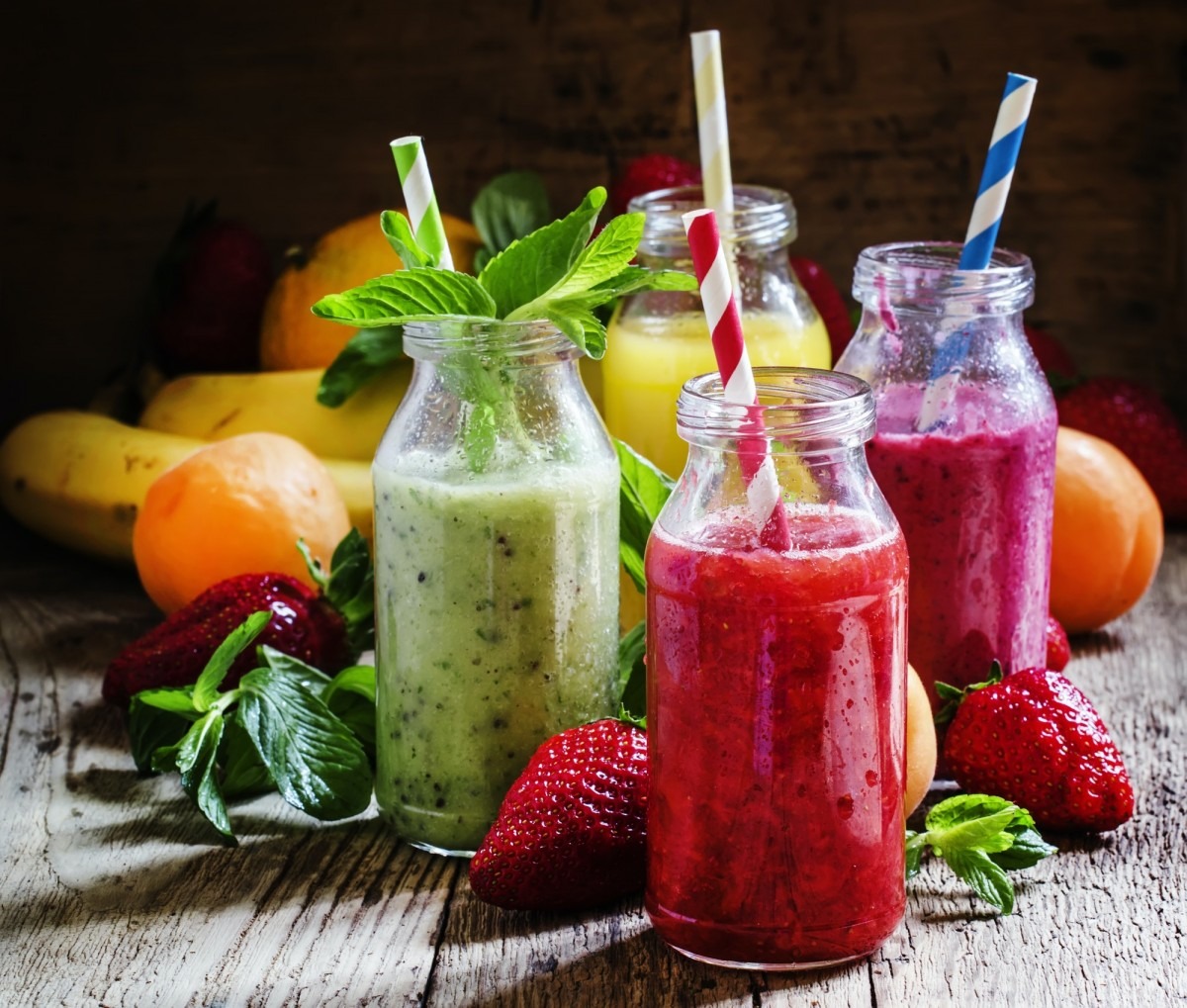 Fruit smoothies with colored straws in glass bottles