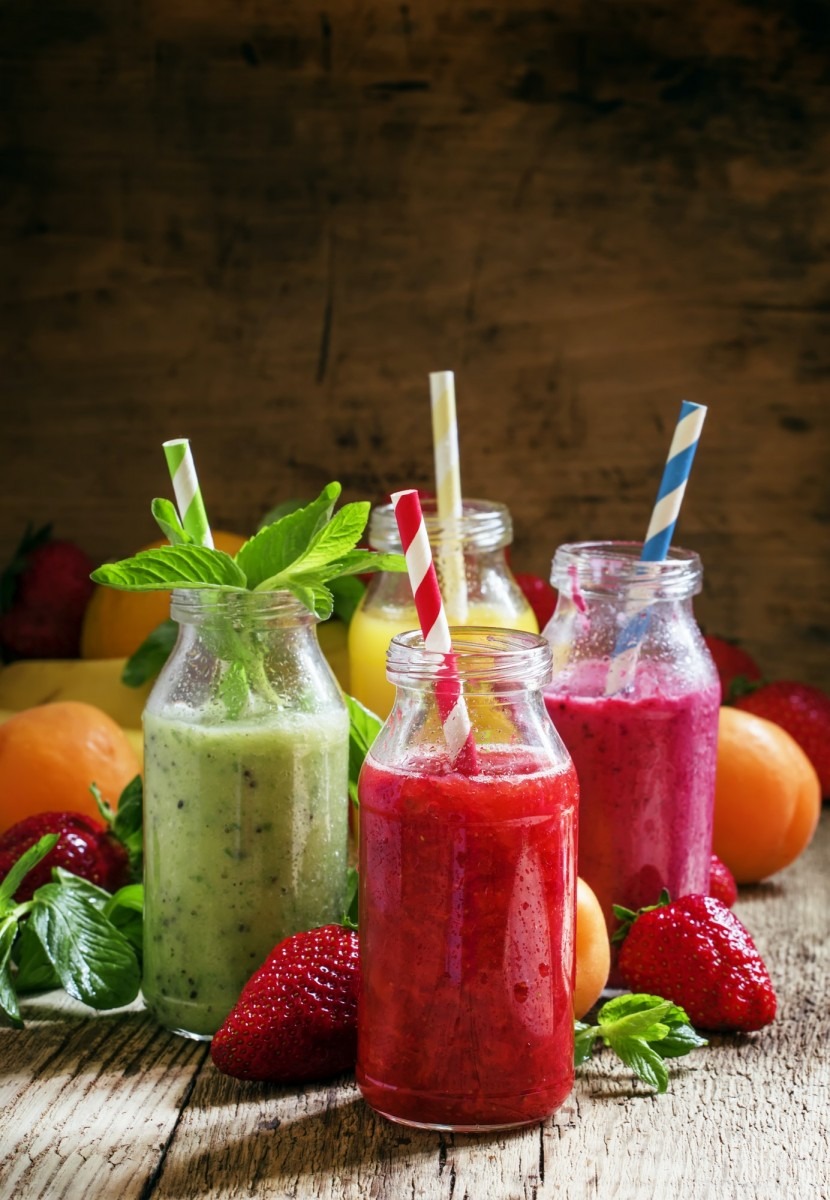 Multi-colored bottles with fresh fruit smoothies with striped straws, berries, fruit and mint Multi-colored bottles with fresh fruit smoothies with striped straws, berries, fruit and mint