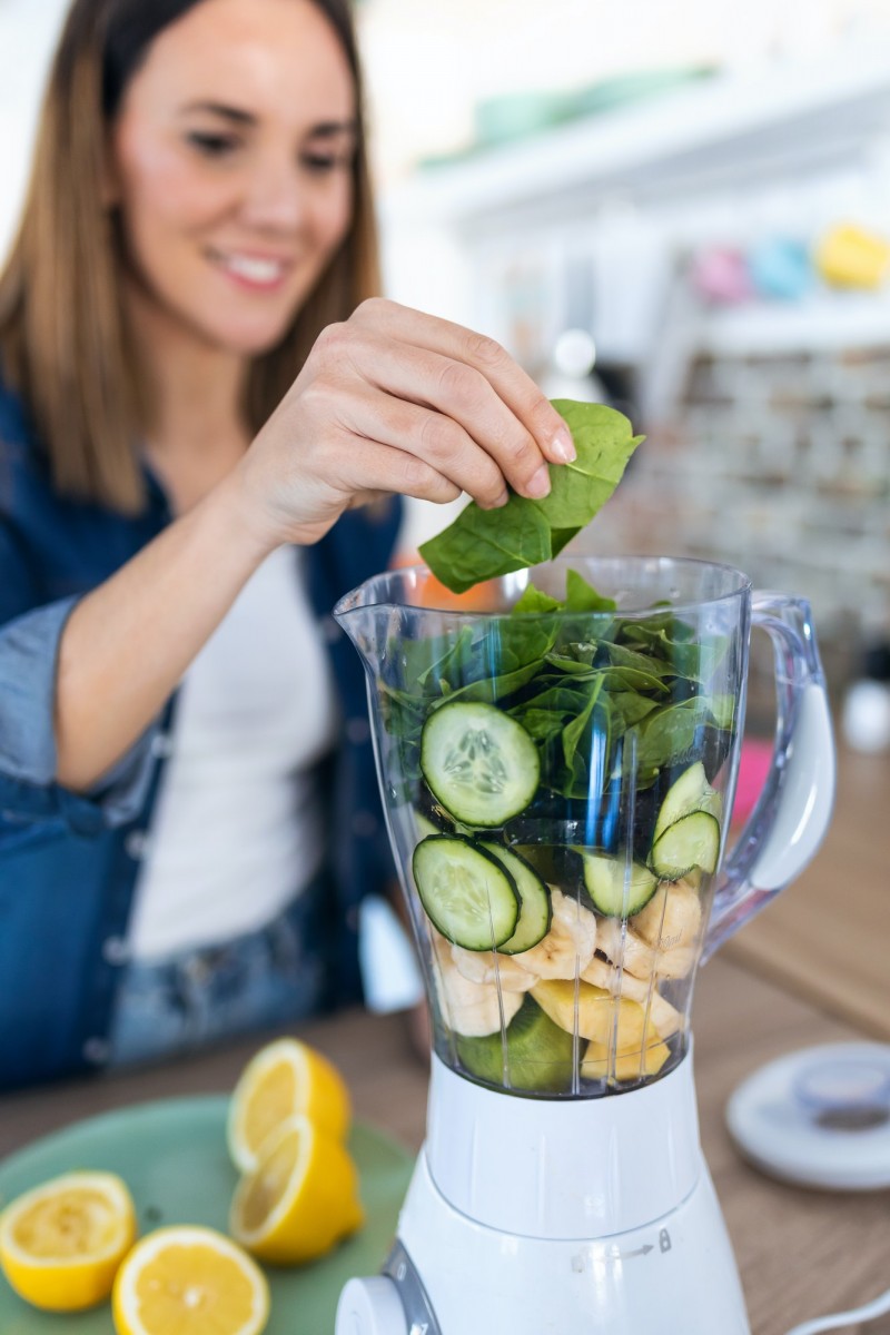 young woman putting spinach in to the blender for preparing detox juice