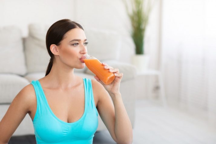 Fitness Girl Drinking Fruit Juice From Bottle Standing At Home