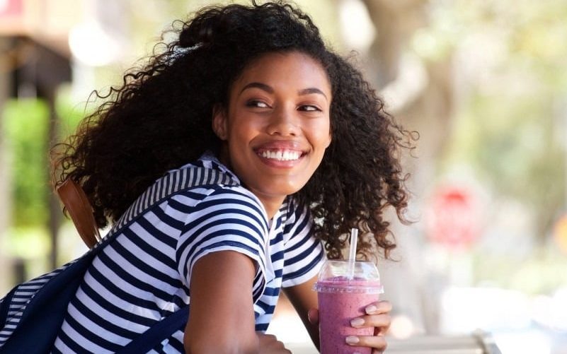 happy young african american woman sitting outdoors holding smoothy drink